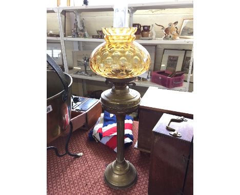 A brass oil lamp with amber tinted glass shade.