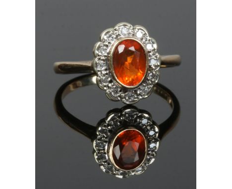 A vintage 9ct gold dress ring with a halo cluster of diamonds and an orange coloured gemstone, size O.