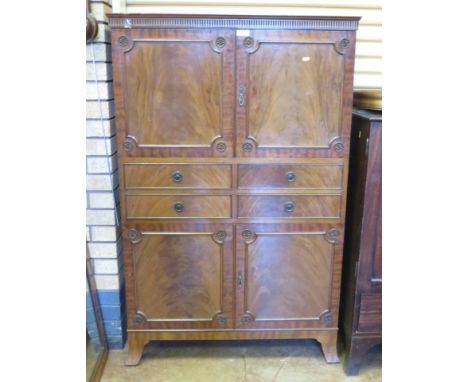 A reproduction mahogany Cabinet with gouge carved frieze, two panelled doors with paterae on corners, four drawers to centre 