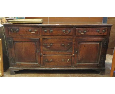An 18th Century oak and elm Dresser Base fitted three frieze drawers, central bank of drawers flanked by two panelled cupboar