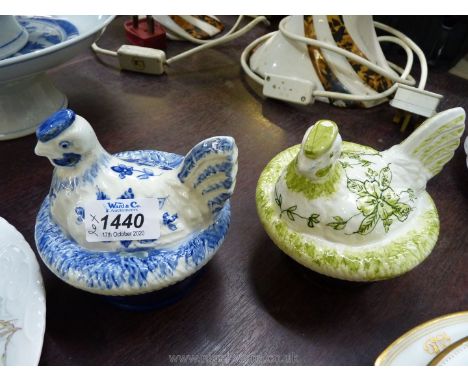 Two small ceramic hens on a nest, one in green, the other in blue.