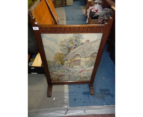 An Oak framed Fire screen having a fluted top rail and with an inset tapestry depicting a thatched cottage with a flagstone p