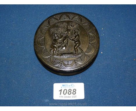 A pressed tortoiseshell circular snuff box decorated with two putti under a tree, holding a bird and basket of eggs.