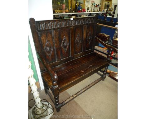 A peg-joyned Oak Settle having four panelled back rest with fluted and carved top rail, standing on turned legs and arm suppo