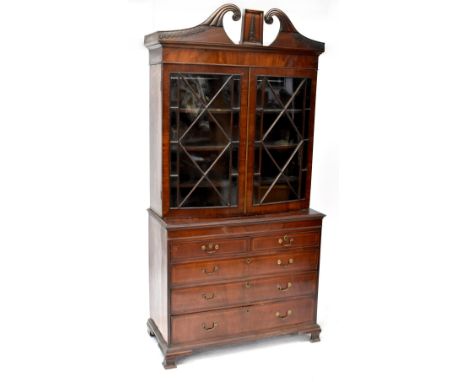 A George III mahogany bookcase, the glazed bow top with broken swan neck pediment and foliate carving, on an associated base 