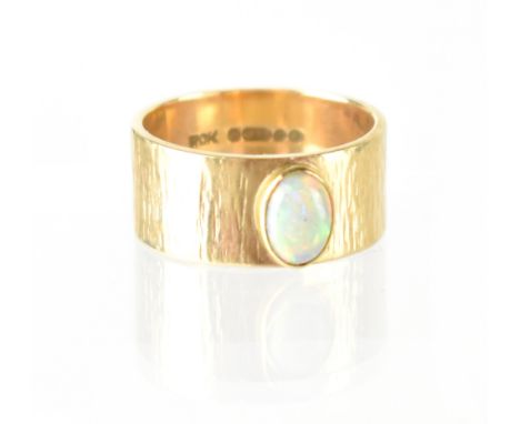 A 1970s 9ct gold contemporary ring of a textured band adorned with an oval white opal in gold bezel, size P, approx 6.4g. CON