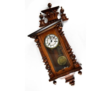 An early 20th century mahogany-cased Vienna-style wall clock, carved pediment to the top above a white enamelled dial set wit