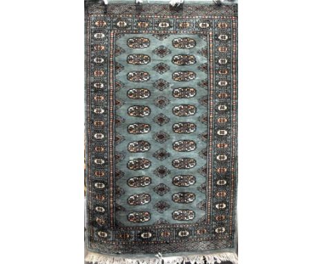 Three hand-knotted rugs from Pakistan to include a pair of jade green ground rugs with lozenge decoration and a pale pink exa