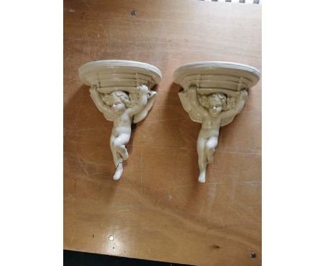 A pair of glazed Poole pottery glazed cherub formed wall shelves. Each approximately 28cm high. Incised marks to the rear. So
