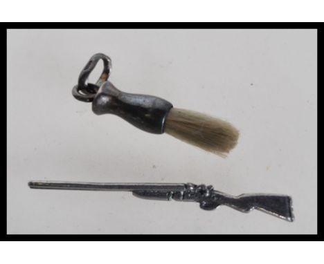 A silver miniature doll's house side by side shotgun along with a miniature brush with a loop finial to the top.&nbsp;