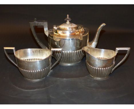 A silver three piece tea set with ribbed repousse decoration with ebonized handle and finial to teapot, Sheffield 1907. weigh