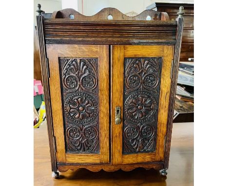 A late Victorian oak smokers cabinet, circa 1900, carved gallery top mounted with skittle finials, fluted frieze above two pa