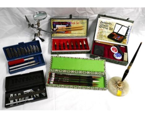 Three boxed Chinese brush and writing sets, 2 boxed scalpel sets, marble based desk stand and a precision magnifying glass.