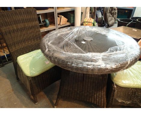 Black rattan circular table with tempered glass top and metal centerpiece. Two chairs with green cushions, all by Ethical Gar