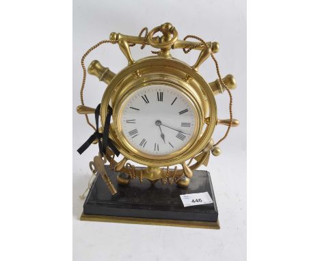 A brass mantel clock shaped as a ships wheel, white enamel dial with black Roman numerals mounted on a black rectangular base