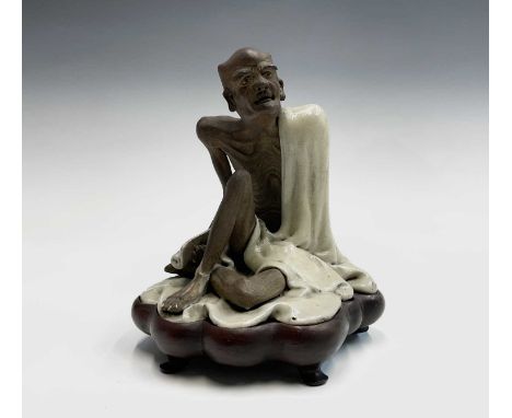 A Chinese Jun-type figure of a seated luohan, Qing Dynasty, holding a scroll in right hand, on a shaped hardwood base, total 