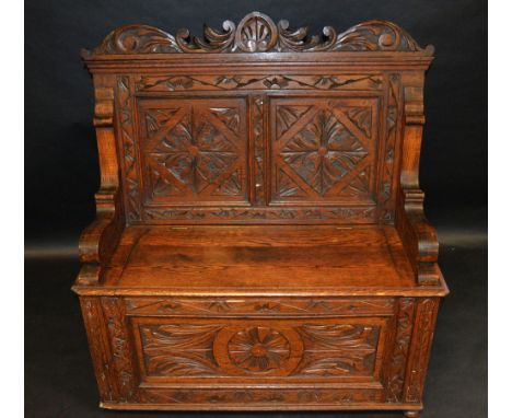 An oak Monk's bench, the back carved with lozenges, scroll arms, hinged seat, the base with roundel and foliage, 106cm high, 