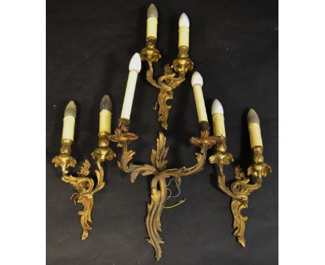 A set of three gilt metal two-light wall lights, leafy sconces and drip pans, cast overall with leafy scrolls, 30cm high;  an