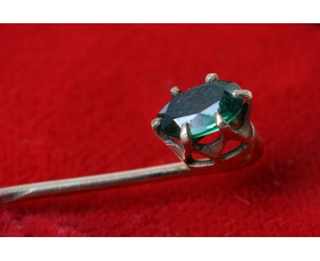 A gold stick pin set with green stone