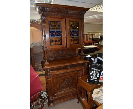 A late 19th Century oak profusely carved cabinet with a pair of lead light doors above a single drawer and cupboard door depi