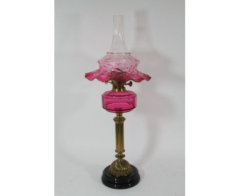 A Victorian oil lamp with cranberry shade and font with fluted column