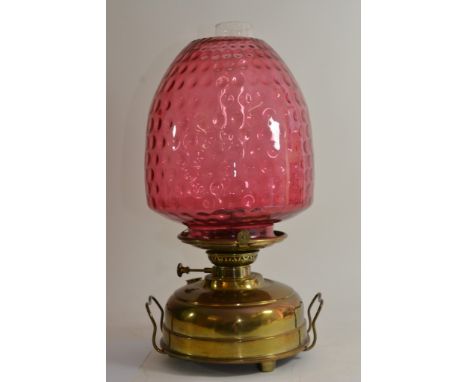 A Victorian oil lamp with a large cranberry glass shade on a brass base