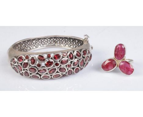 Two pieces of silver jewellery; consisting of a hinged bangle with pierced decoration, half set with red stones and a floral 