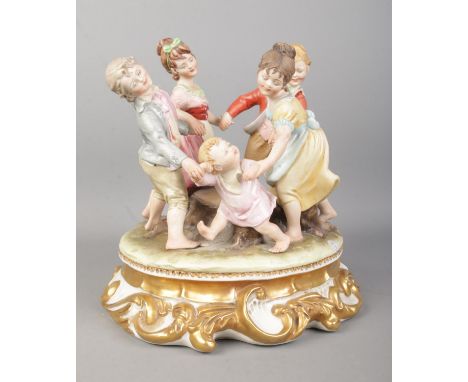 A Capodimonte figure group 'Ring A Roses' depicting children in a circle surrounding a tree trunk. Raised on gilt highlighted