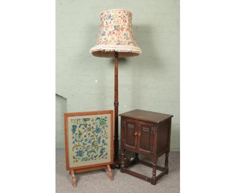 A small carved linen fold cabinet along with a turned mahogany standard lamp and an embroided firescreen.