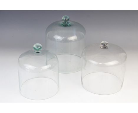 Three clear-glass cloches, late 19th/early 20th century, each of typical bell-shaped form below a moulded button handle, tall