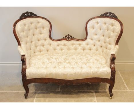 A Victorian mahogany framed double spoon back sofa, the shaped button back applied with carved leafy open work crests, extend