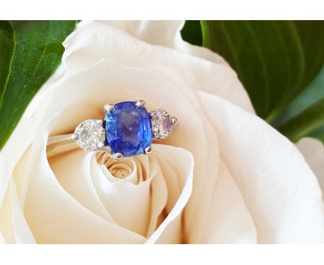 A sapphire and diamond three-stone ring, the (untested) central mixed, cushion cut sapphire (measuring 6.98mm x 6.03mm), with