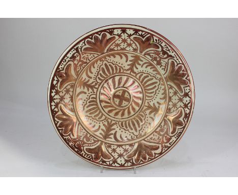 A Spanish pottery lusterware charger, with stylized foliate decoration in light relief, in dark red on cream ground, marked J