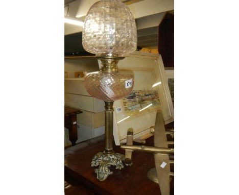 A brass column oil lamp with pink tinted font and shade.