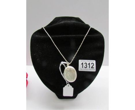 A vintage silver oval locket with lightly cut work to back and front of flowers and leaves on a silver chain.