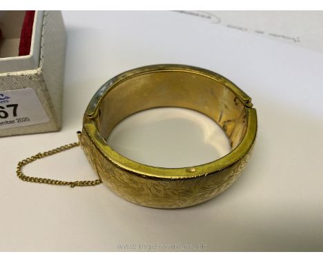 A boxed yellow metal hollow bangle with press action latch and safety chain and decorated with stylised flowering plants stam