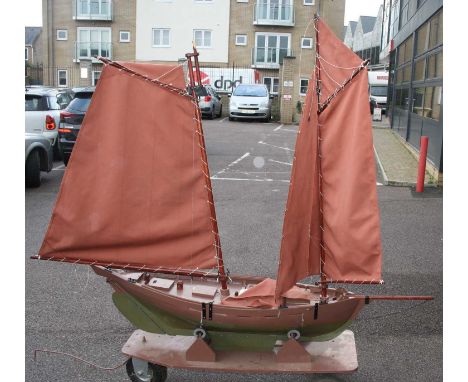 A wooden scratch-built model of a large scale sailing yacht, complete with twin masts and red canvas sails, with removable de