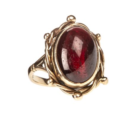 RED GEM SET RING, the oval cabochon red gem 13mm long, within a ropetwist border with spherical terminals, marked 9ct, size J
