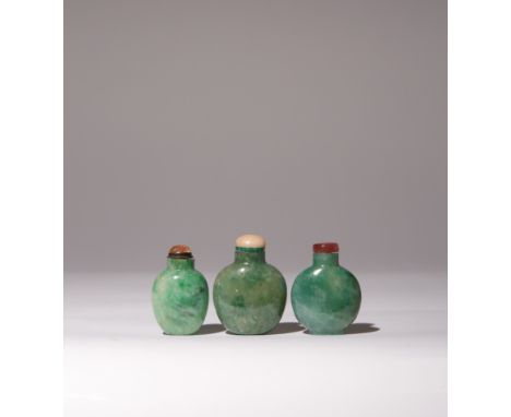 THREE CHINESE JADEITE SNUFF BOTTLES QING DYNASTY Each of flattened ovoid shape, the apple-green stones with flecks of emerald