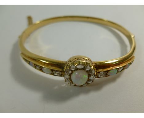 A late Victorian gold, opal and diamond hinged bangle, the oval opal and rose cut diamond central cluster with ornate scrolli