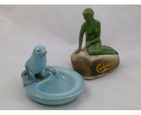 A pottery 'Carlsberg' advertising item in the form of a nude lady seated on a rock, 17cm high and a blue glazed dish in the f