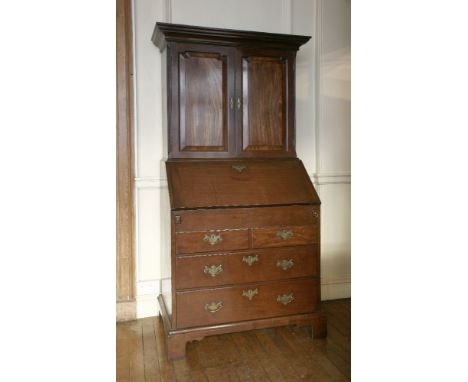 A George III mahogany bureau cabinet,the top section with a moulded cornice over two shaped panelled doors, enclosing shelves