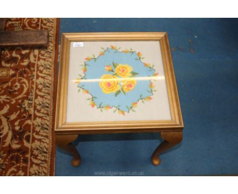 A small square wooden table having a tapestry floral top covered with glass.