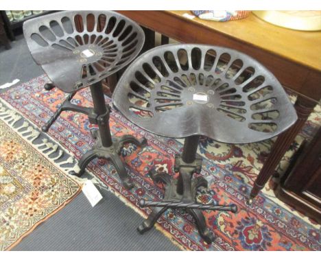 A pair of cast iron adjustable bar stools with tractor style seats