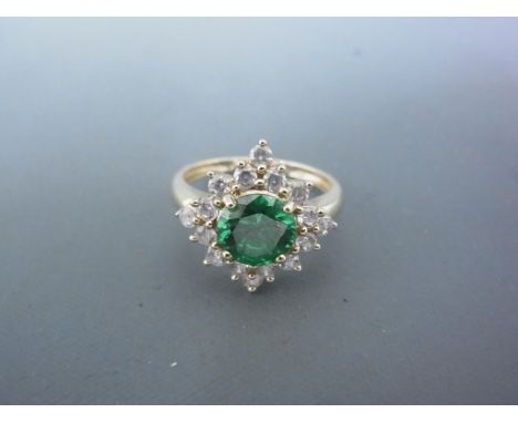 A 14ct yellow gold dress ring with large circular cut green stone surrounded by sixteen small circular clear stones - ring si