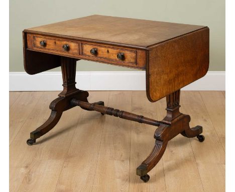 A George III mahogany sofa table, the end supports and carved reeded legs united by a turned stretcher all on brass casters, 