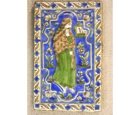 An antique Qajar Persian hand painted and polychrome glazed ceramic tile depicting a man in traditional robes within a stylis