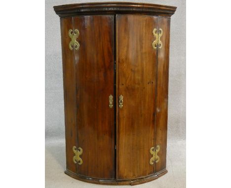 A Georgian mahogany bowfronted corner cabinet with dentil cornice above panel doors with original hinges on plinth base. H.10