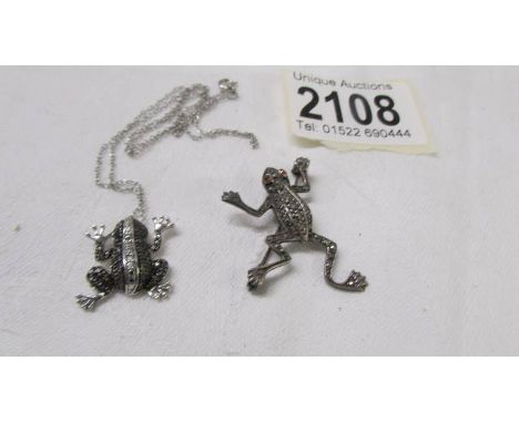 A silver frog pendant on a silver chain and a silver frog brooch.