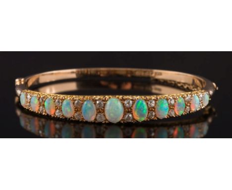 An early 20th century gold, opal and diamond mounted hinged bangle: with eleven graduated opals separated by pairs of graduat